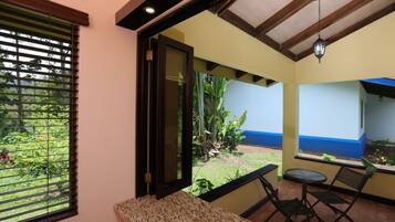 A room with a view of a garden, a sliding door, a small table with chairs, and a ceiling fan.