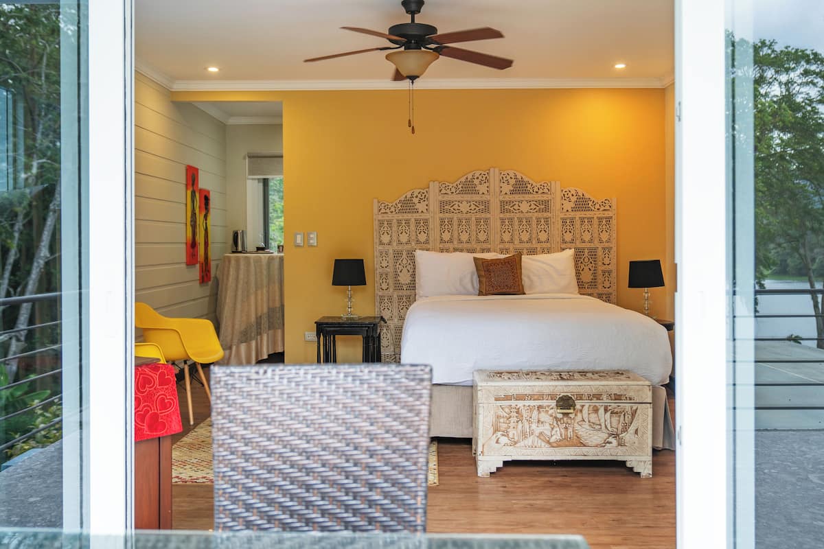 A bedroom with a bed, bedside tables, a ceiling fan, and a view of the outdoors.