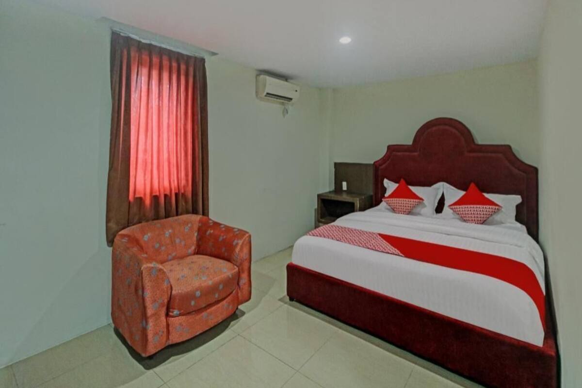 A hotel room with a bed, a chair, an air conditioning unit, and a nightstand.