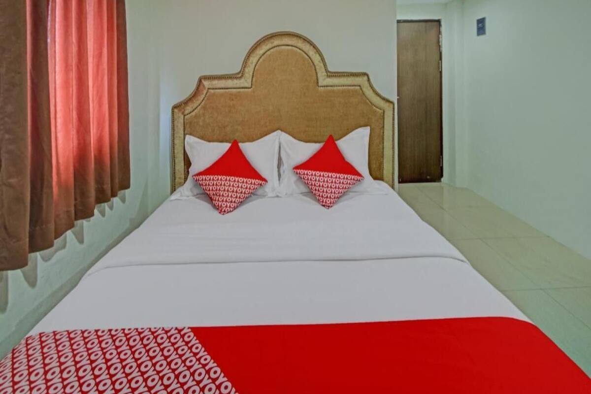 A hotel room with a bed, red and white pillows, a red and white bedspread, and a wooden headboard.