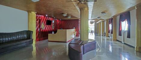 A spacious lobby with a reception desk, a seating area, and a ceiling with chandeliers and a fan.