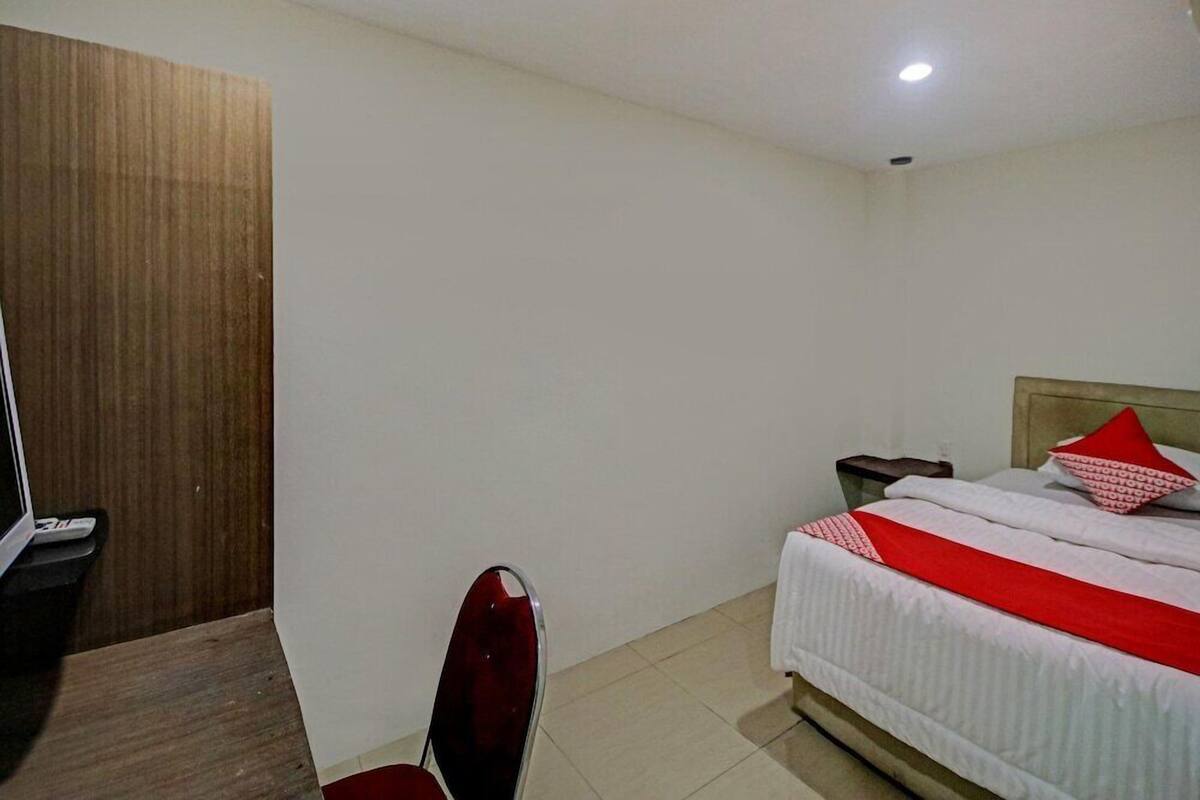 A hotel room with a bed, a desk, a chair, a wooden wardrobe, and a nightstand.