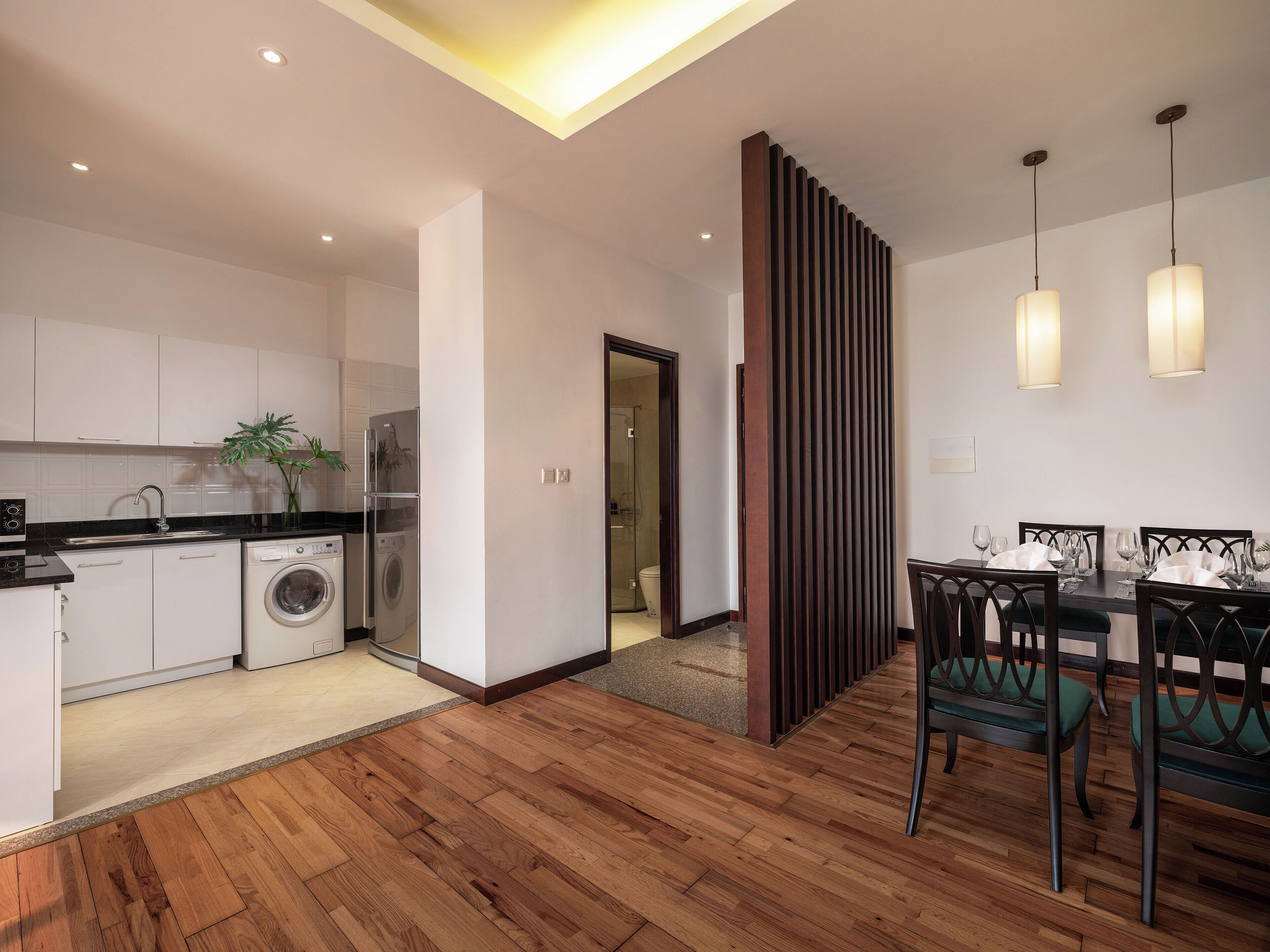A modern kitchen with a washing machine, a dining area with a table set for four, and a wooden floor.