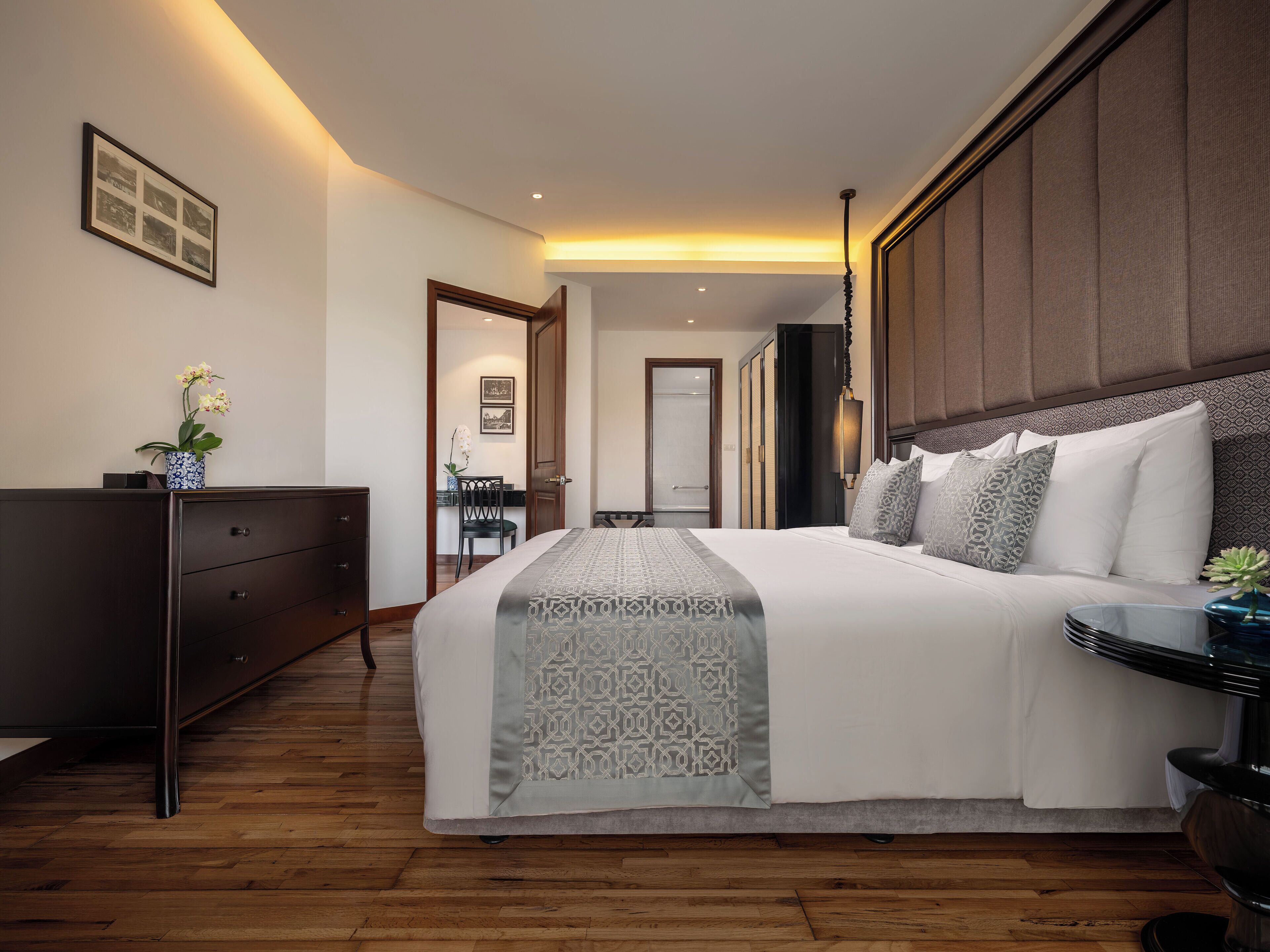 Habitación de hotel moderna con una cama grande, un aparador de madera oscura, un escritorio con una silla y vistas al pasillo.