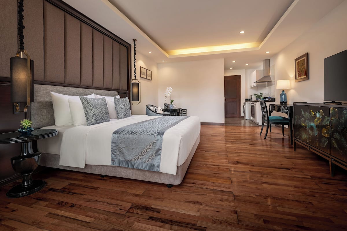 A hotel room with a large bed, a desk, a chair, a TV, and a kitchen area.