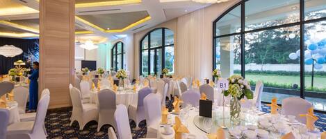 A banquet hall with round tables set for dining, white chairs, and a large chandelier.