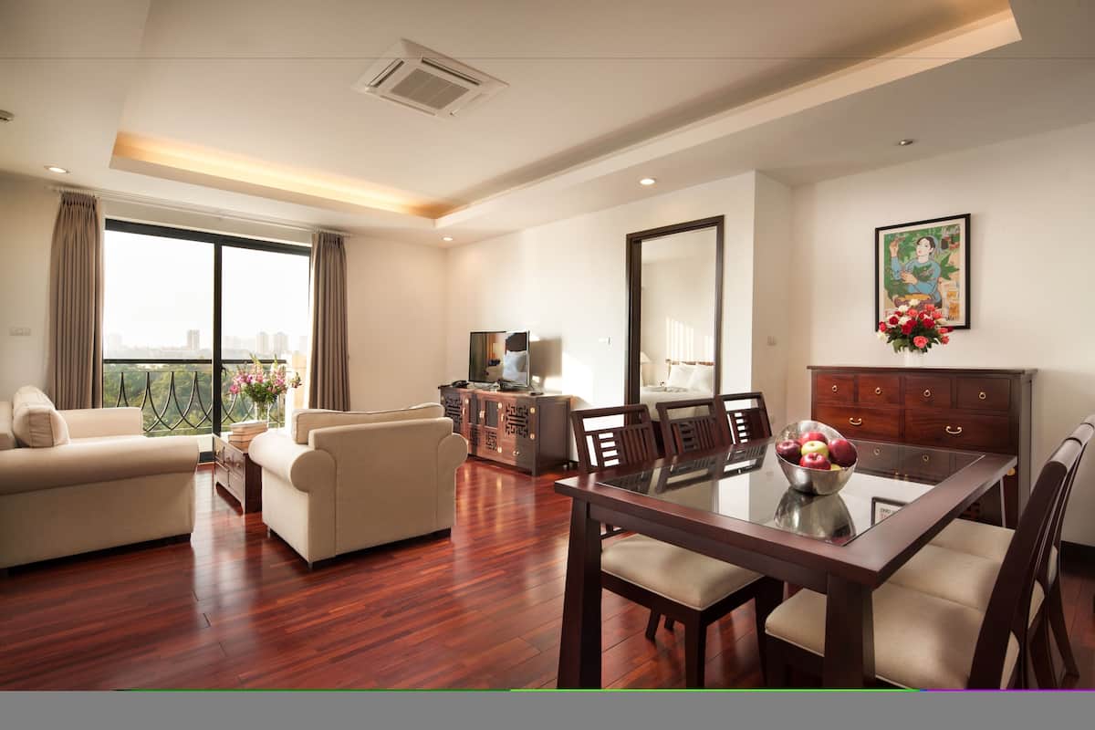 A spacious living room with a wooden floor, a dining area with a glass table, and a balcony with a city view.