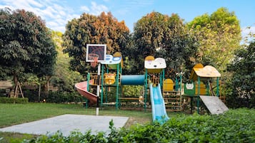 A playground with slides and climbing structures, surrounded by trees and a clear sky.