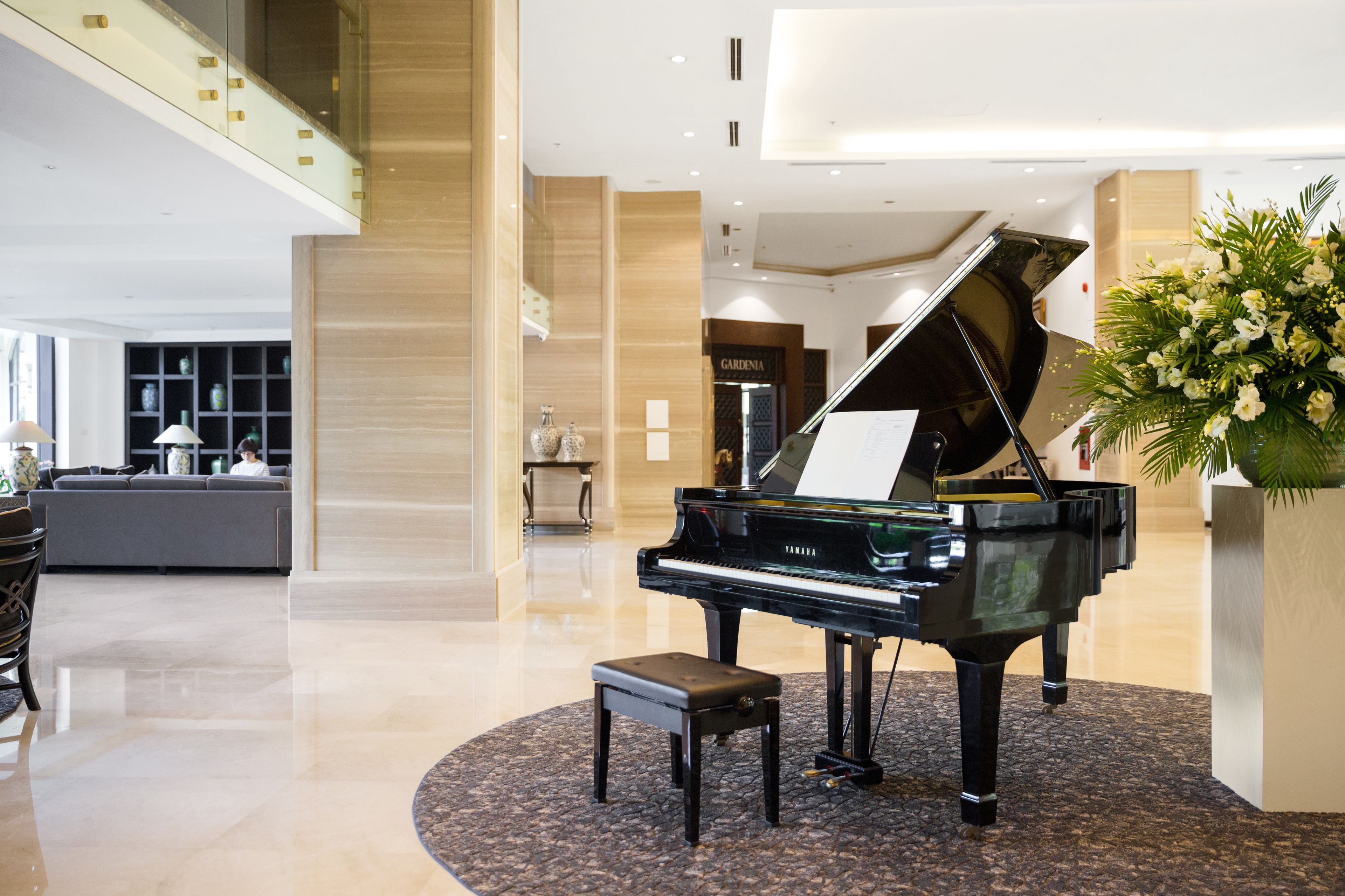 A grand piano in a spacious lobby with a high ceiling, a seating area, and a decorative plant.