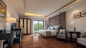 Un dormitorio amplio con una cama grande, un escritorio, una silla y un balcón con vistas a zonas verdes.