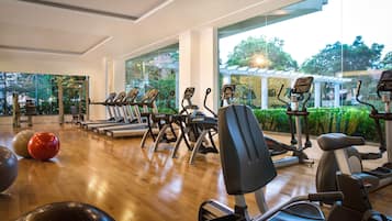 Een sportschool met cardioapparatuur, trainingsballen en uitzicht op een tuin door grote ramen.