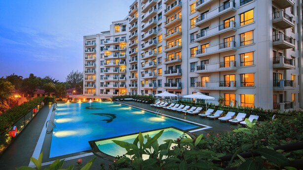 Un hotel de varios pisos con piscina, sillas de descanso y balcones.