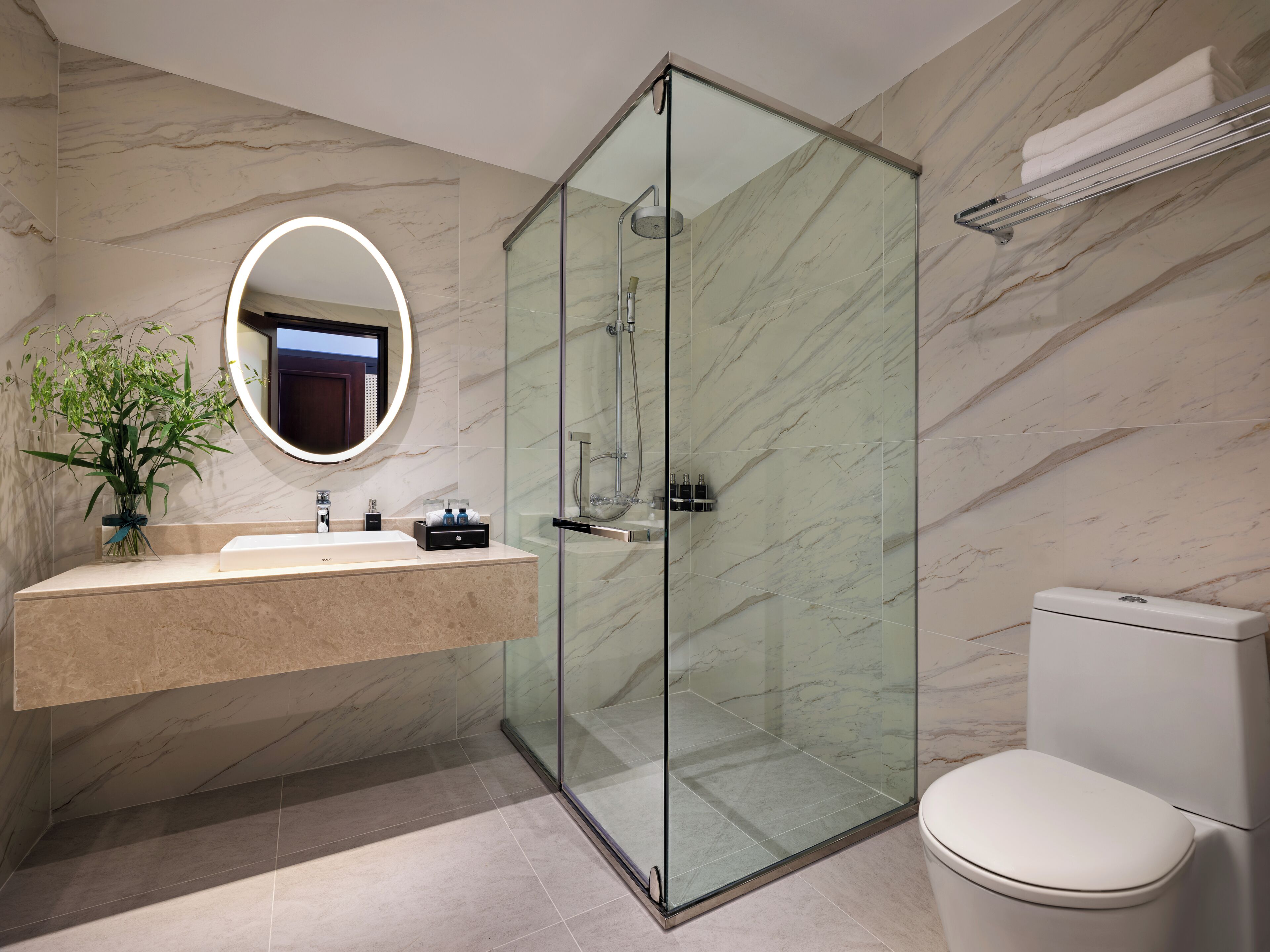 A modern bathroom with a glass-enclosed shower, a marble-tiled wall, a sink with a mirror, and a toilet.