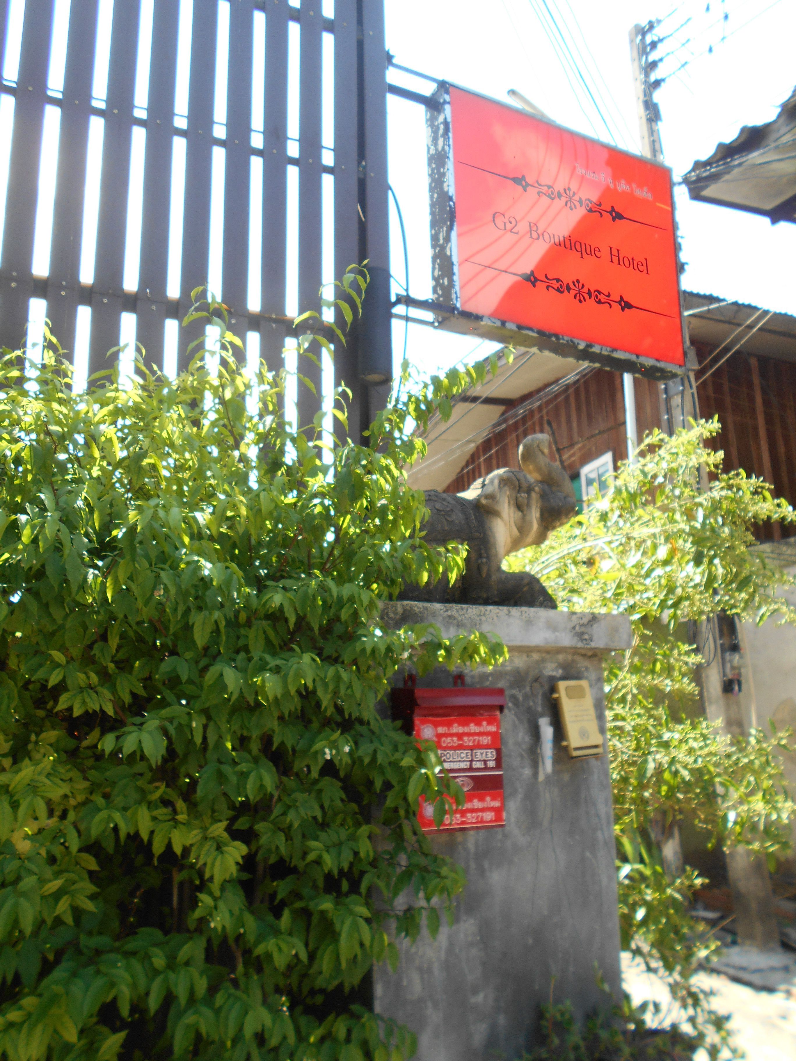A red sign for G2 Boutique Hotel, a metal statue, and a red emergency call sign.