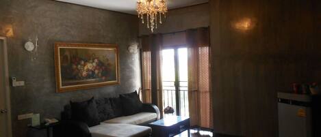 A living room with a sofa, a chandelier, a painting, and a window with curtains.