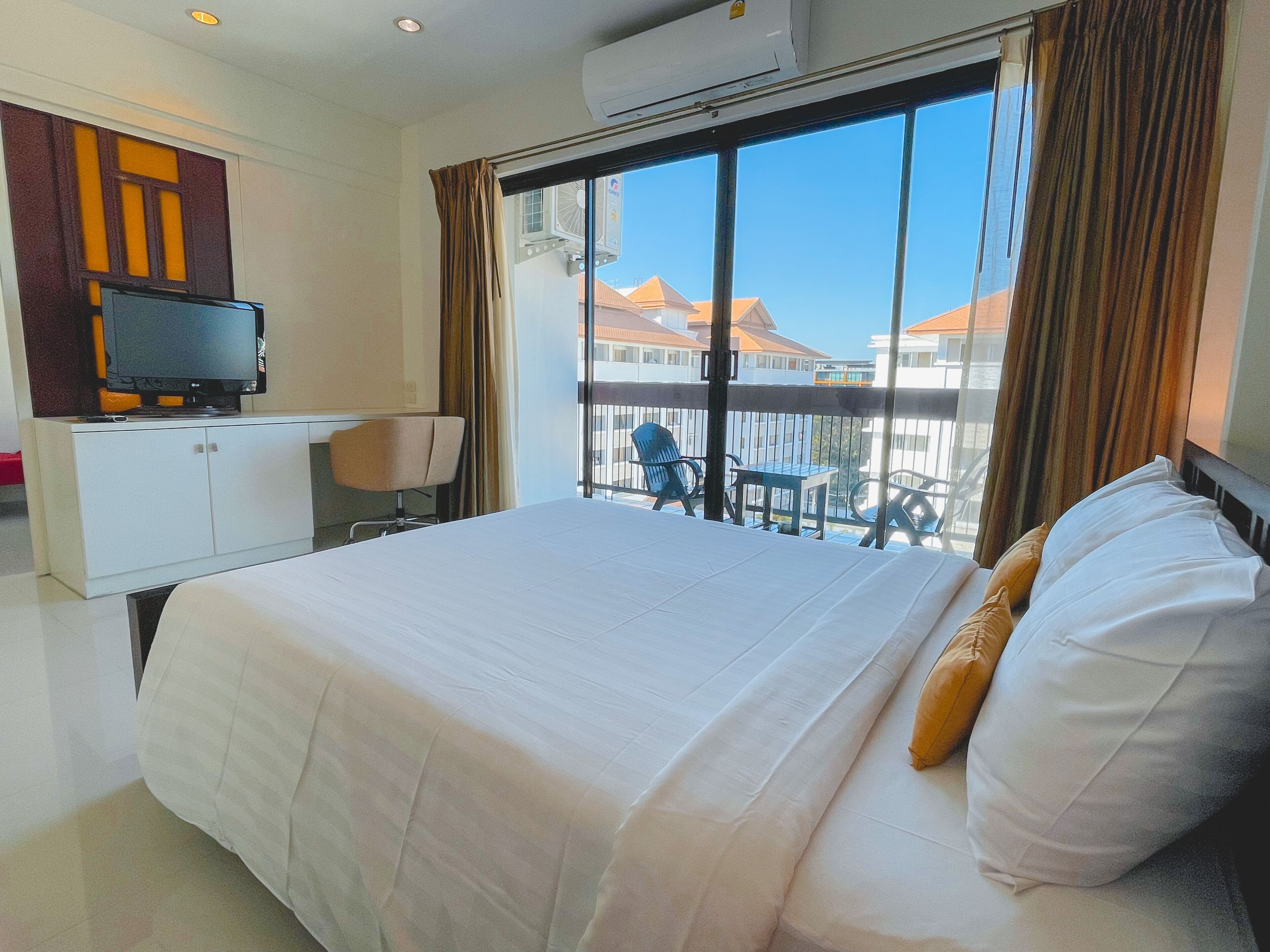 A hotel room with a large bed, a desk with a television, and a balcony with a view of buildings.
