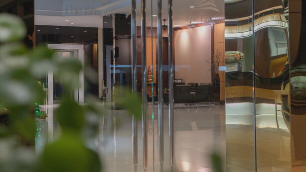 A modern hotel lobby with a glass partition, a reception desk, and a staircase. - The Empire Nimman (Chiang Mai)