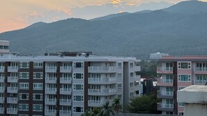 A multi-story residential building with balconies, set against a backdrop of mountains and a sunset. - The Empire Nimman (Chiang Mai)
