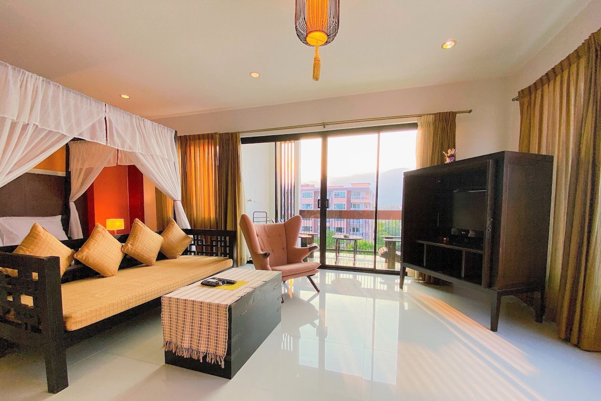 A hotel room with a bed, sofa, TV, and a balcony with a view.