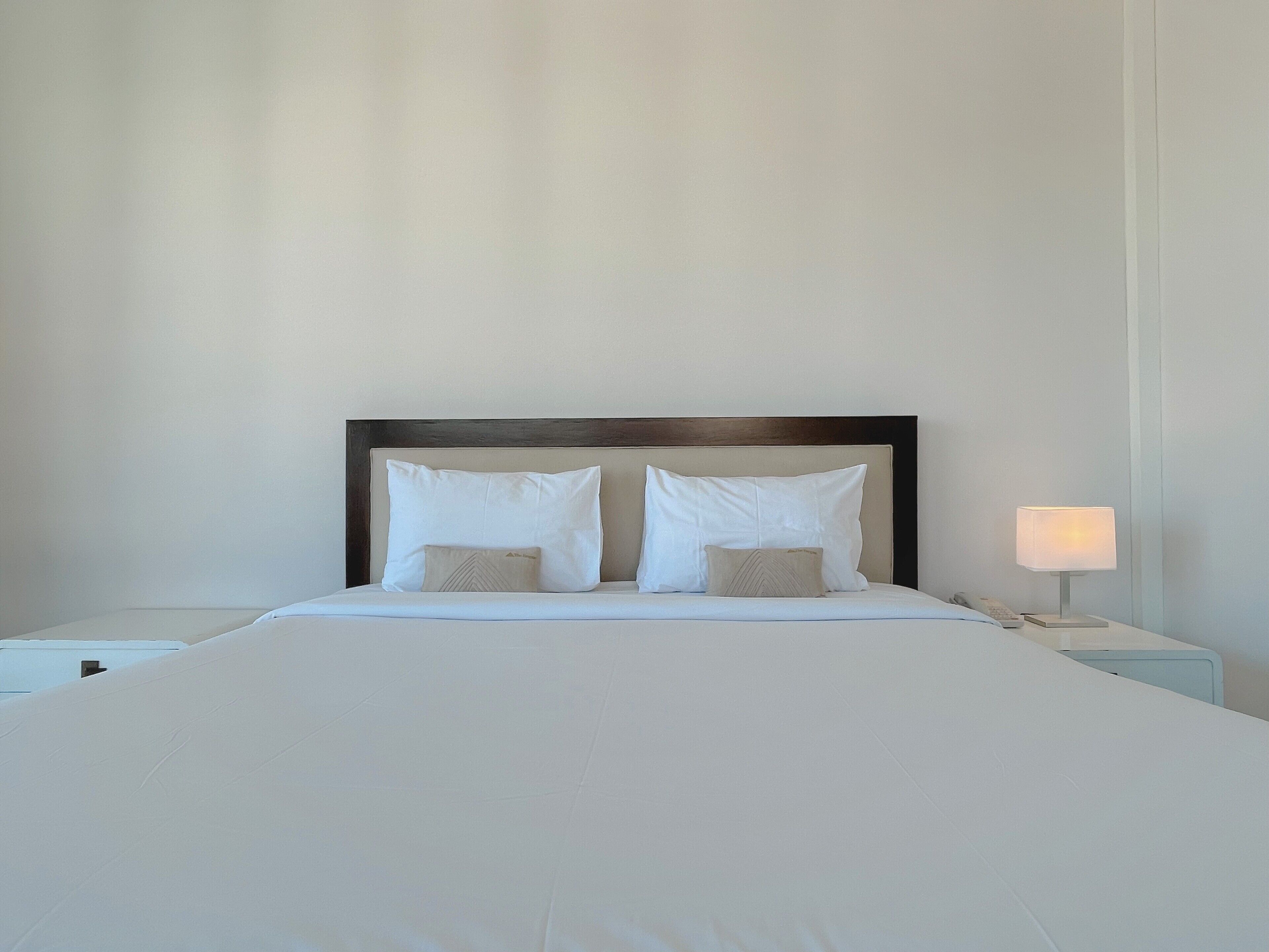 A neatly made bed with a wooden headboard, two white pillows, and a bedside lamp.