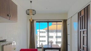 A modern living room with a red sofa, a dining table, and a view of buildings through large windows. - The Empire Nimman (Chiang Mai)