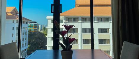 A room with a large window, a table with a potted plant, and a view of buildings.