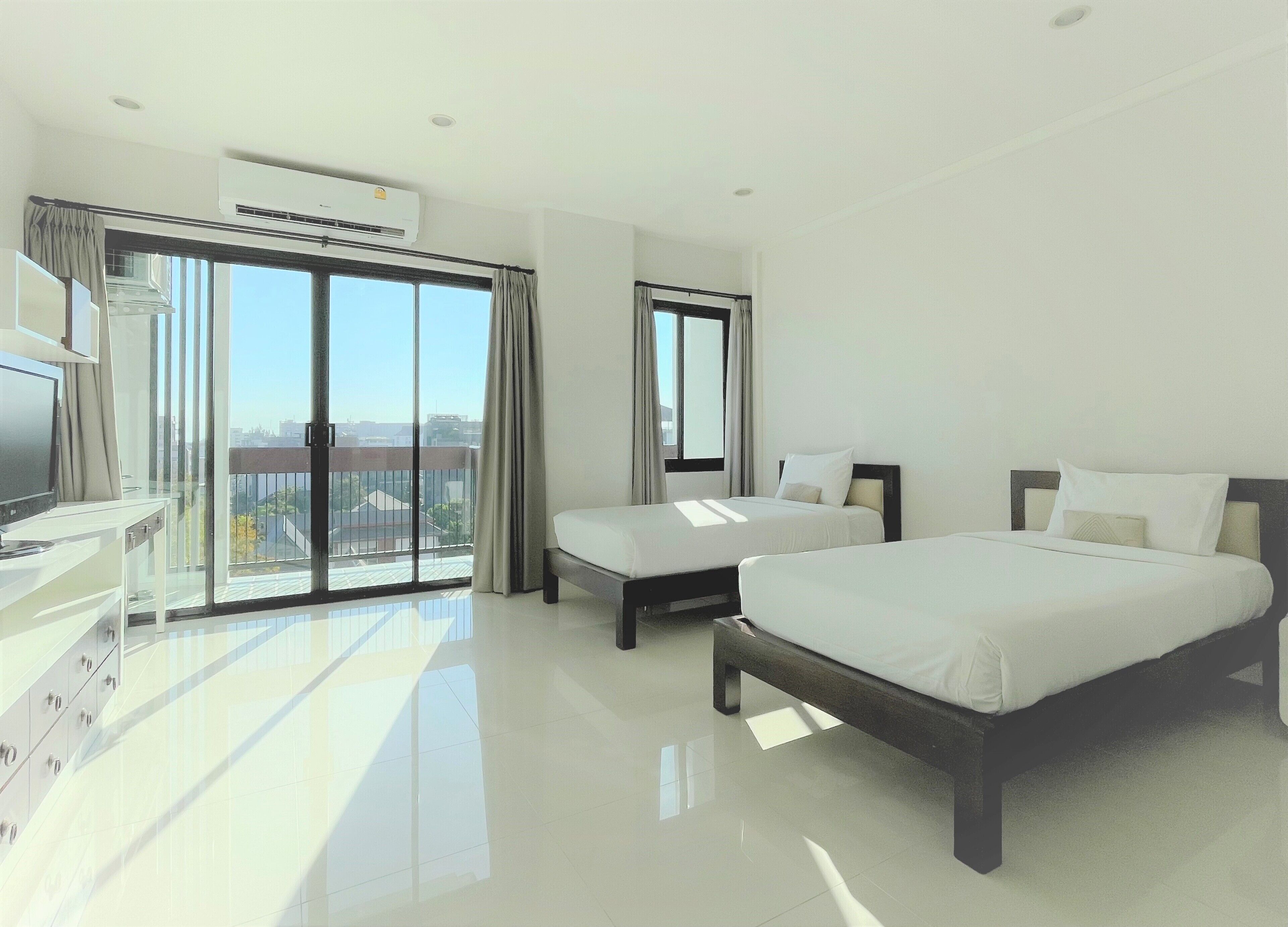 A modern hotel room with a large bed, a smaller bed, a desk with a chair, and a television.
