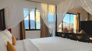 A hotel room with a large bed, a TV, and a view of the mountains through the windows. - The Empire Nimman (Chiang Mai)