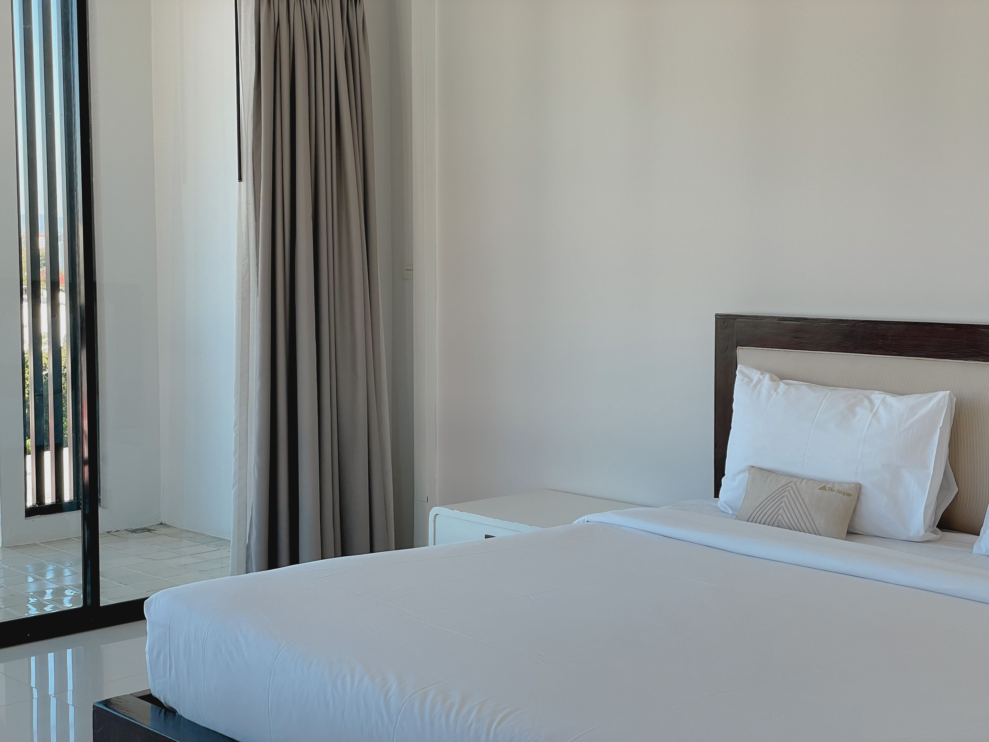 A hotel room with a bed, bedside tables, a headboard, and a view through a window with curtains.