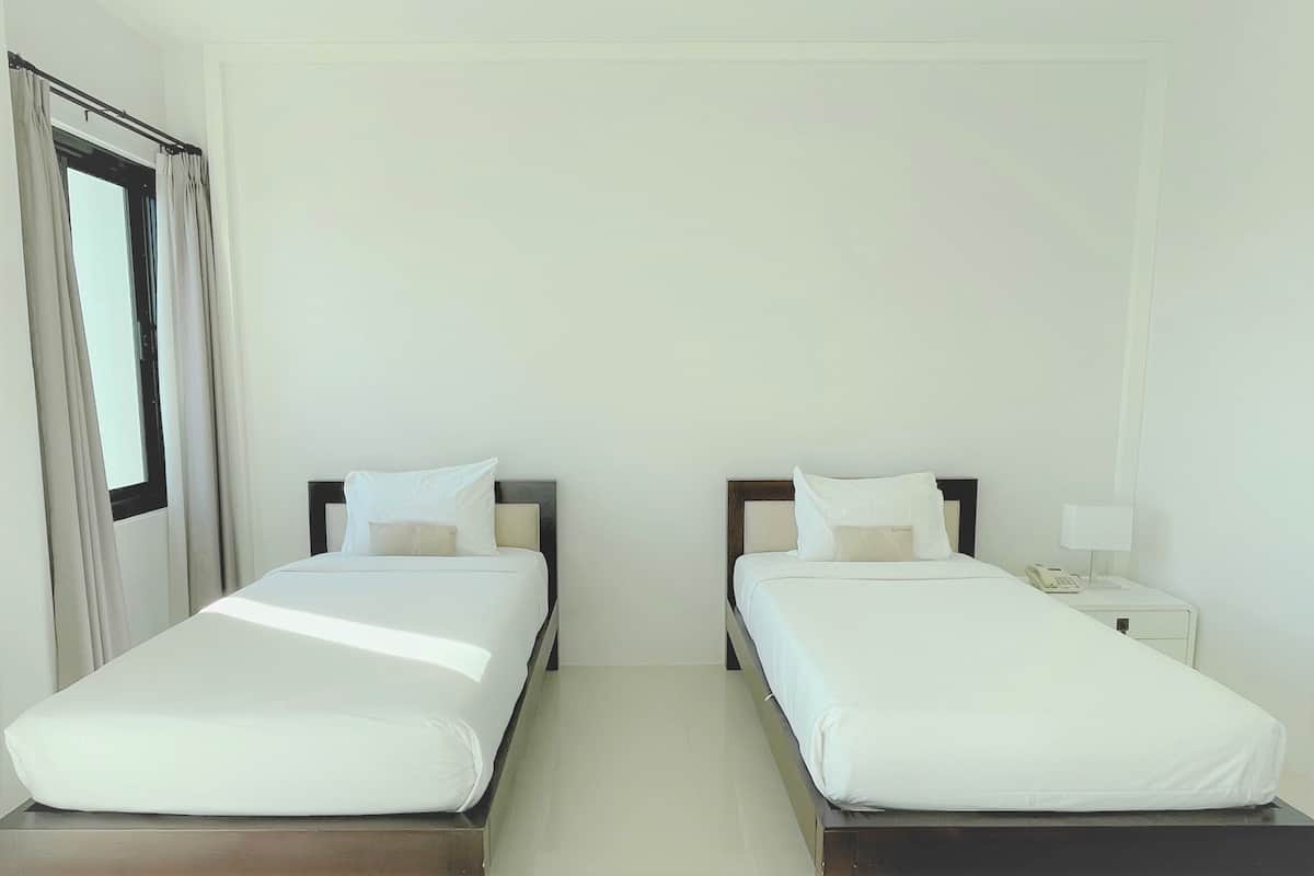 A hotel room with two single beds, a nightstand with a lamp, and a window with curtains.