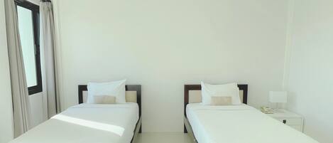 A hotel room with two single beds, a nightstand with a lamp, and a window with curtains.