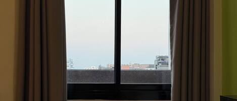 Een hotelkamer met een bed, gordijnen en een raam met uitzicht op gebouwen.