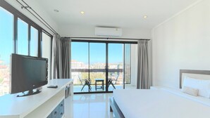 A hotel room with a bed, a TV on a desk, a balcony with a table and chairs, and large windows. - The Empire Nimman (Chiang Mai)