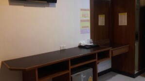 Un escritorio de madera oscura y alargado con un refrigerador pequeño, un televisor de pantalla plana montado en la pared y una puerta con un aviso.