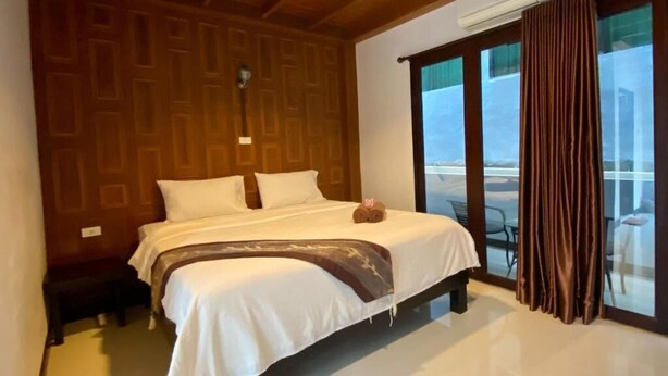 Habitación de hotel con techo de madera, una cama grande con ropa blanca, un banco al pie de la cama y vistas a través de un ventanal.