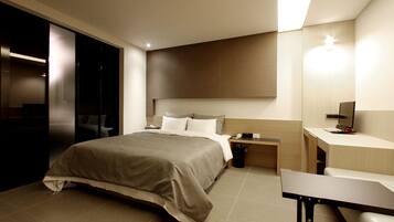 A modern hotel room with a large bed, bedside table, and a desk with a chair.