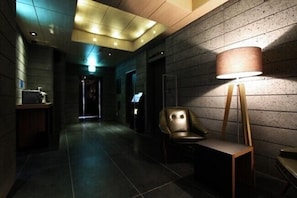 A hallway with a wooden floor, a chair, a lamp, and a wall-mounted light fixture. - Boutique Hotel K Oido (Siheung)