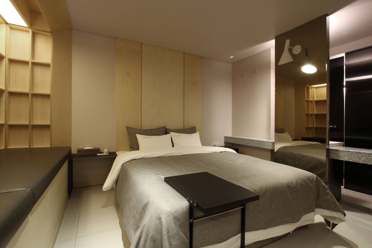 A modern hotel room with a large bed, bedside tables, a built-in wardrobe, and a mirror.