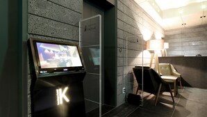 Uma área de recepção moderna com um quiosque digital, um balcão de atendimento e um espaço de espera com luminária e cadeiras.