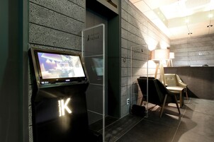 Un área de recepción moderna con un quiosco digital, mostrador de recepción y zona de estar con lámpara y sillones.