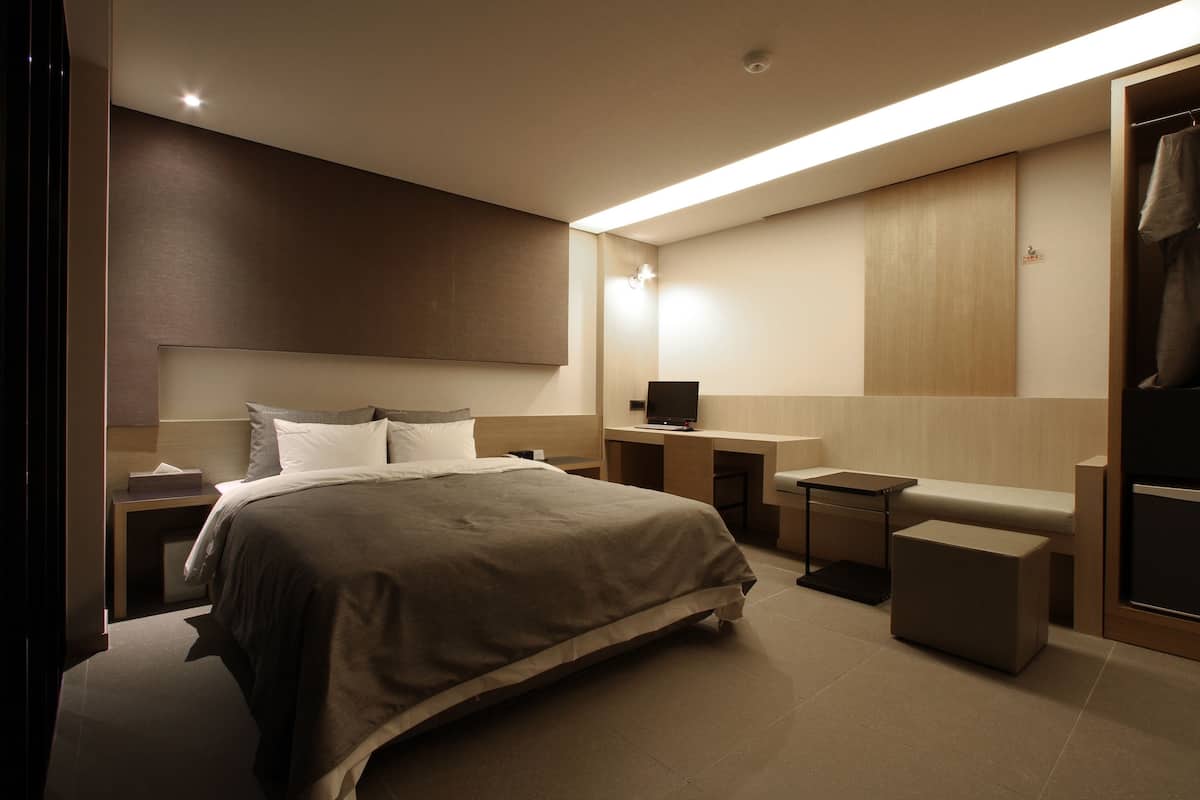 A modern hotel room with a large bed, bedside tables, a desk, and a seating area.