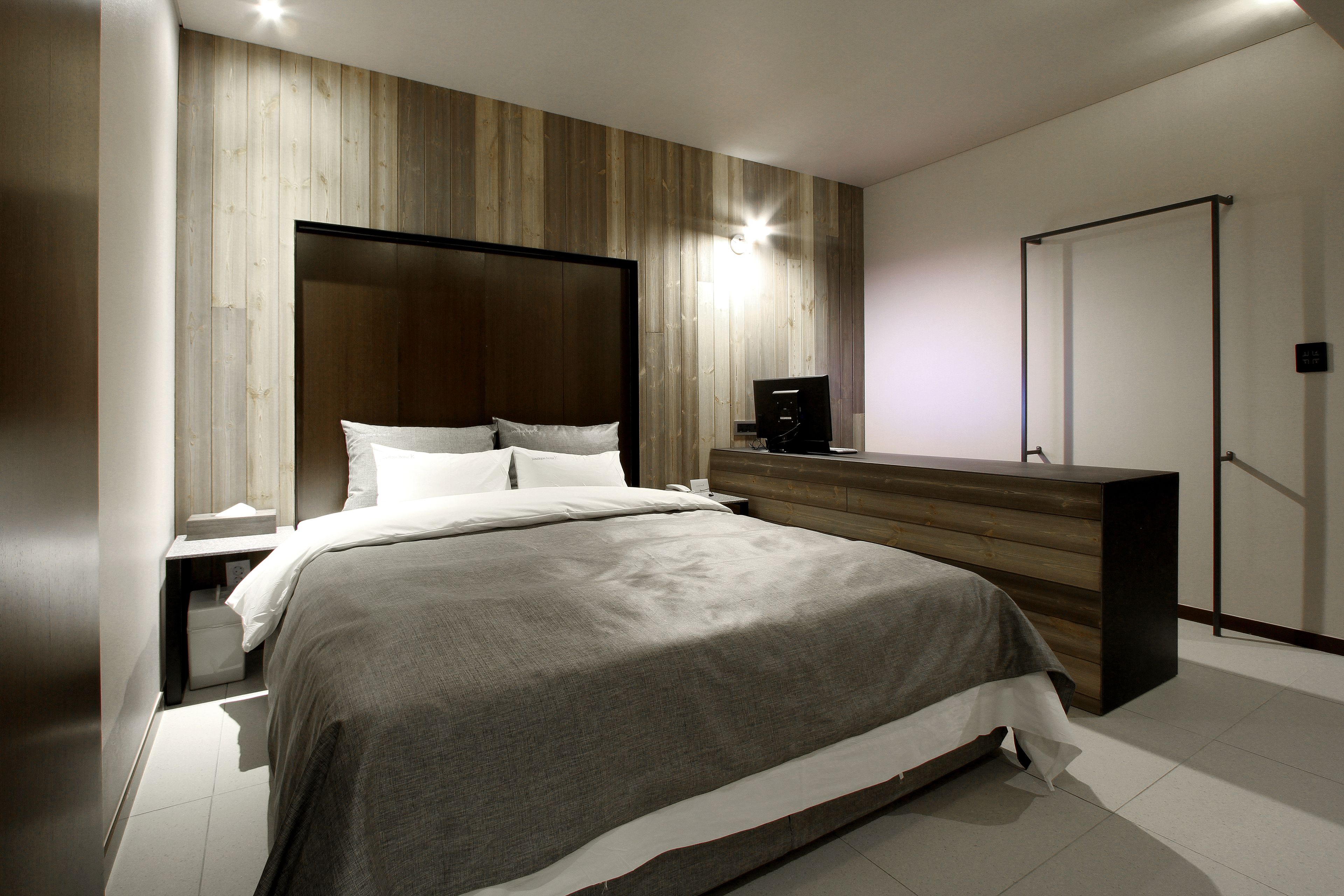 Une chambre moderne avec une tête de lit en bois, un grand lit avec du linge de lit blanc, une table de chevet et un banc intégré.