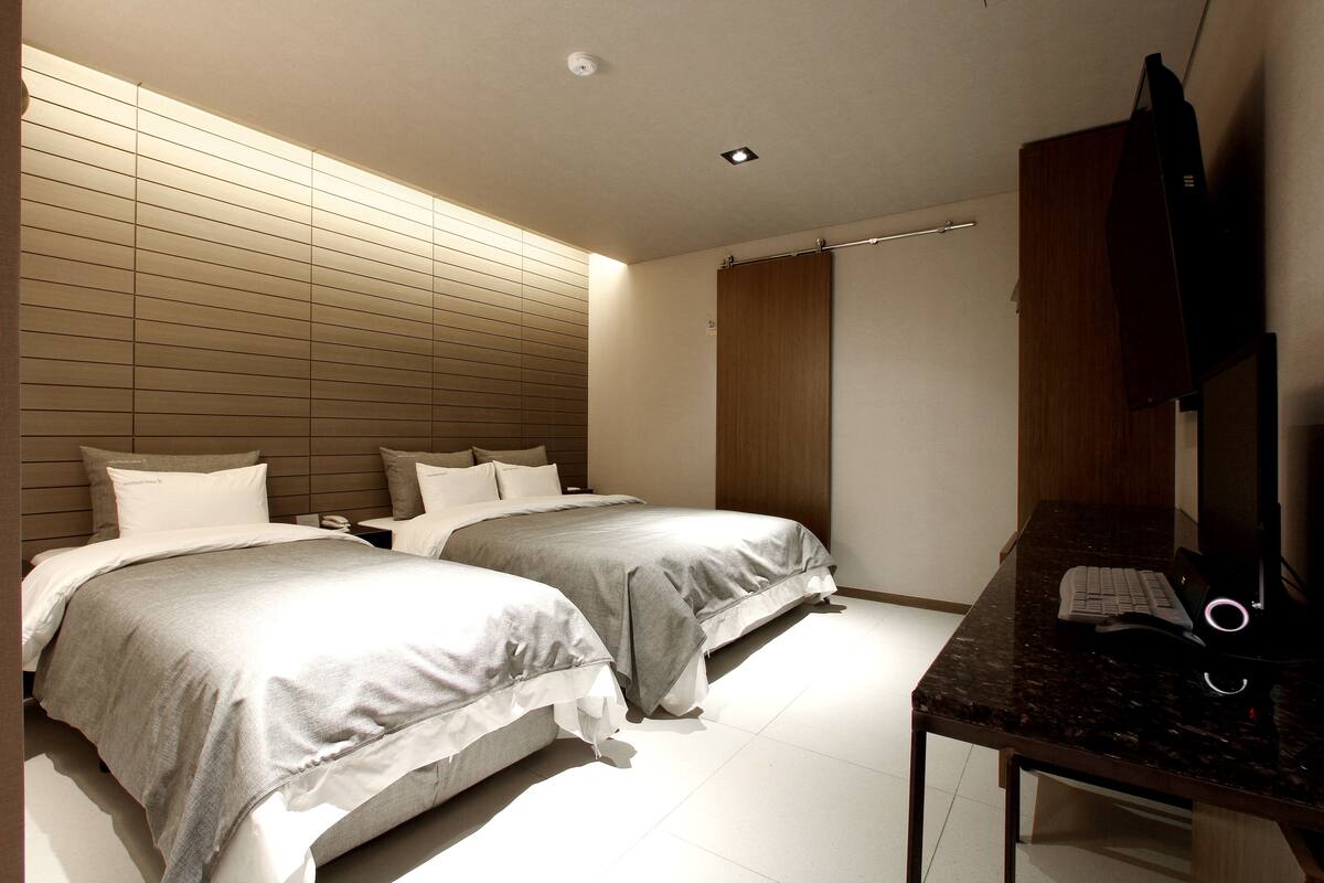 A modern hotel room with two beds, a desk, and a flat-screen TV.