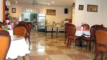 Un restaurante con suelo a cuadros, sillas y mesas de madera. Hay un refrigerador y un reloj en la pared.
