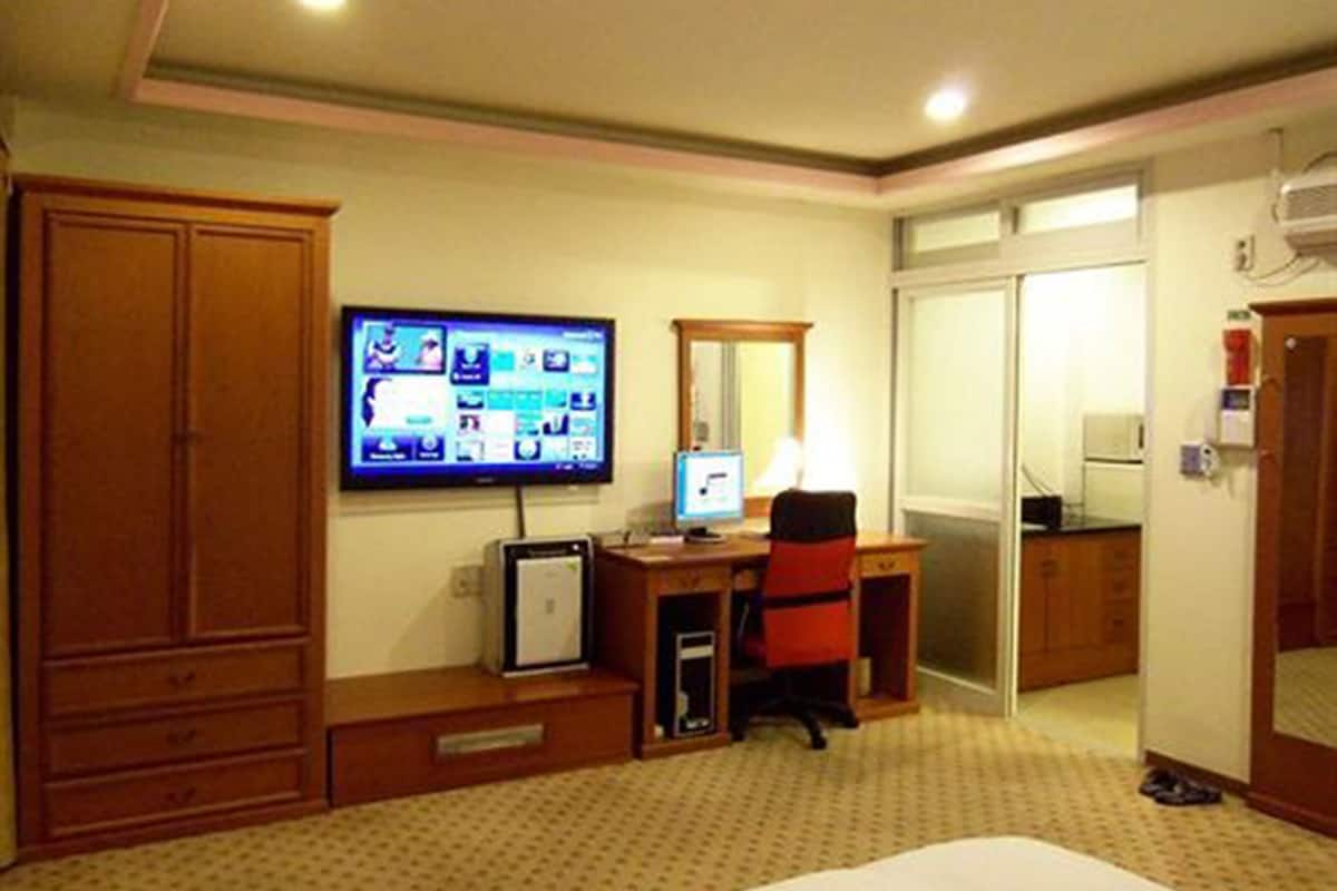 A hotel room with a bed, a desk with a computer, a television, a mirror, and a wardrobe.