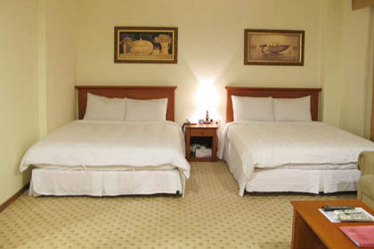A hotel room with two beds, a nightstand, a lamp, and two framed pictures on the wall.