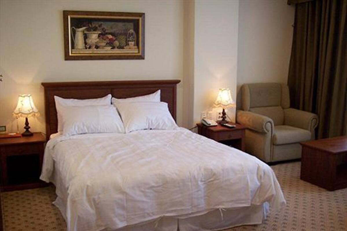 A hotel room with a large bed, two bedside tables with lamps, a chair, and a painting on the wall.