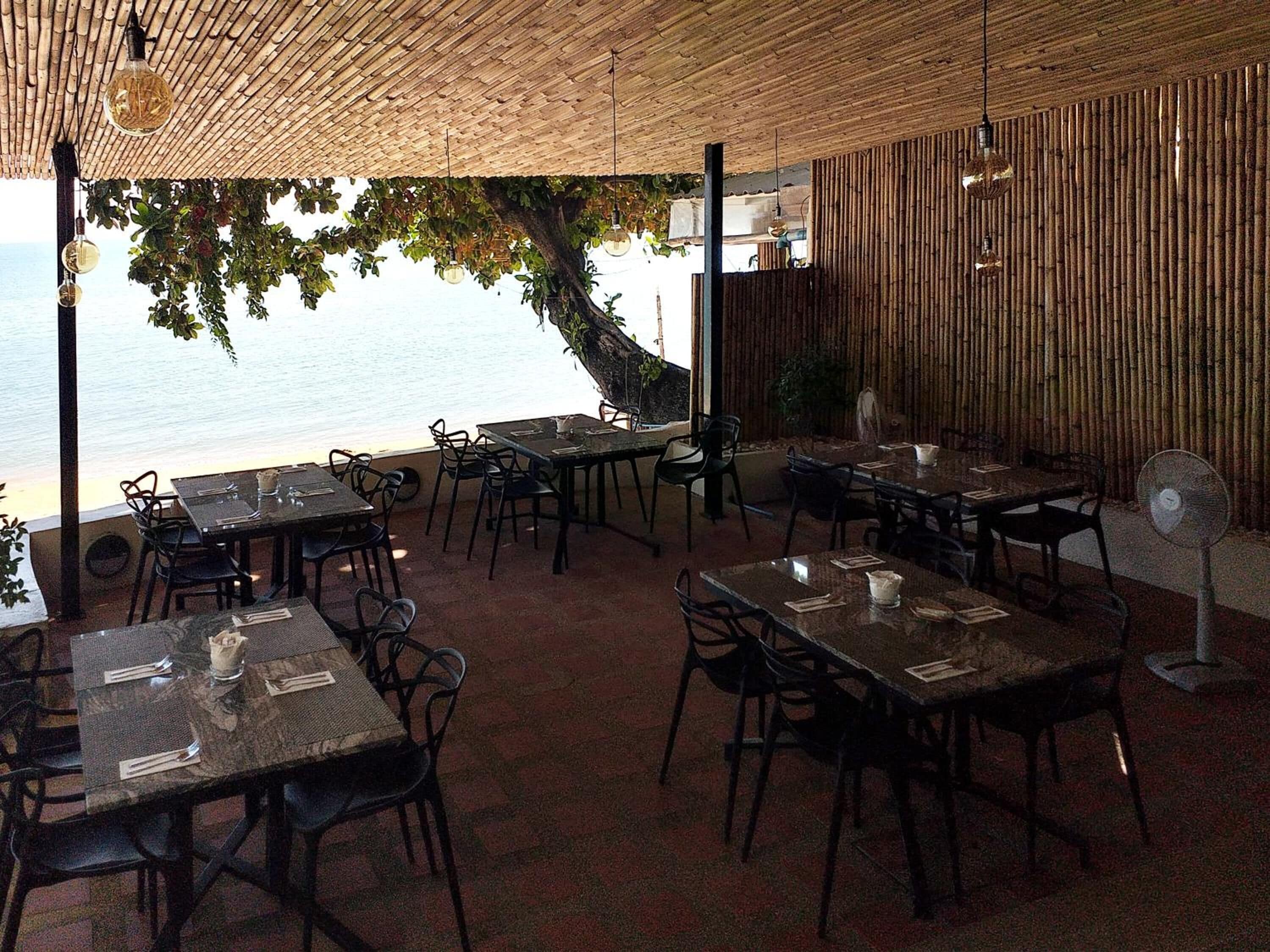 Un área de comedor al aire libre con mesas y sillas, con vistas a un cuerpo de agua.