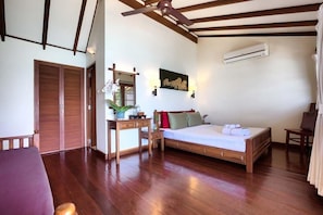 Ein Schlafzimmer mit einem hölzernen Bett, einem Schreibtisch mit Stuhl, einem Deckenventilator und einer Klimaanlage.