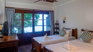 A hotel room with two beds, a desk, a chair, a ceiling fan, and a window with curtains. - The Lodge (Koh Samui)